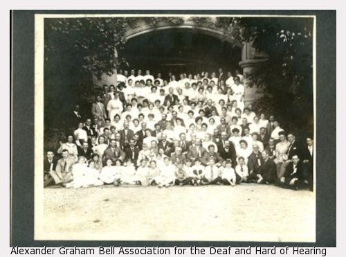 Large black and white group photo taken under an archway of the American Association to Promote Teaching Speech to the Deaf Summer Meeting in 1908.