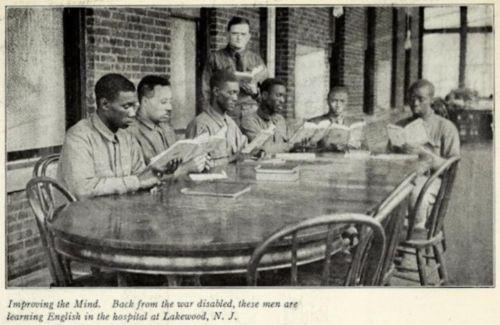 Six African American men sit around a table while a white man in uniform looks on.