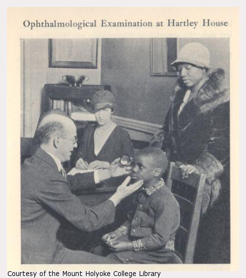Doctor examines the eyes of an African American boy, two women look on.