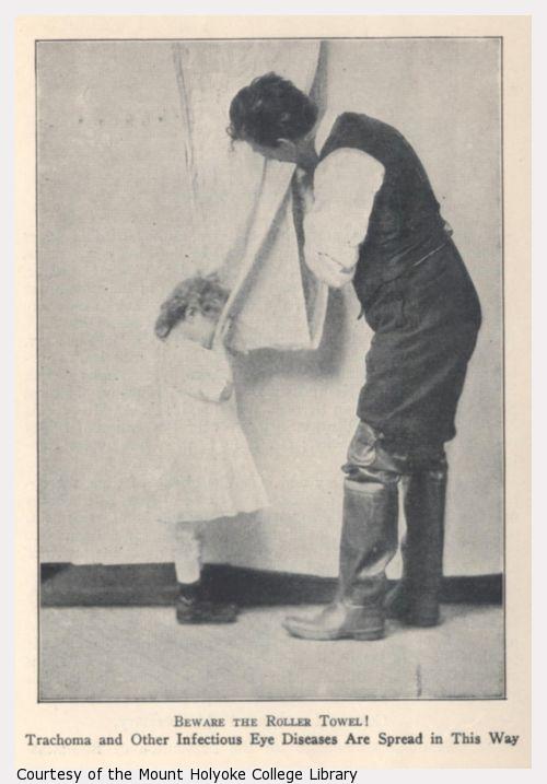 Small child dries hands and face with a roller towel also used by a man.