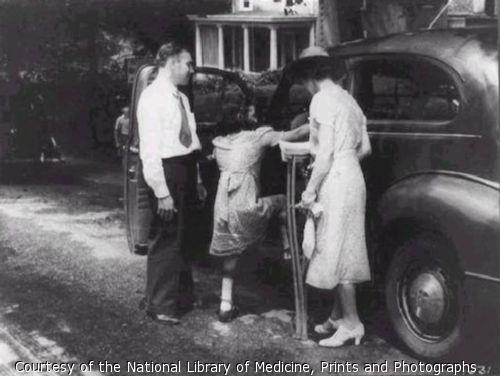 Little girl with braces on her legs climbs into car; man stands to her left and a woman, holding crutches, stands to her right