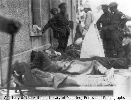 Soldiers lying on stretchers; nurse and officers in background