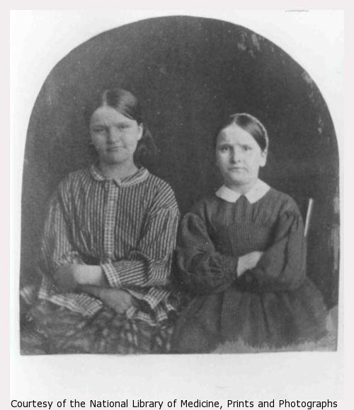 Two women pose with their arms crossed against their chests