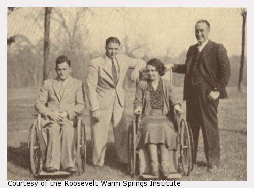 A man and and woman in wheelchairs with two men standing.