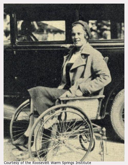 A woman sits in a wheelchair next to a car.