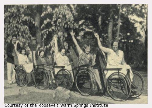 Five women in a row of wheelchairs, the last pushed by a young man.